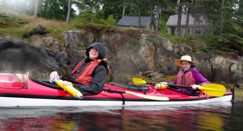 Two people wearing life jackets sit inside a kayak and smile for the photo. 